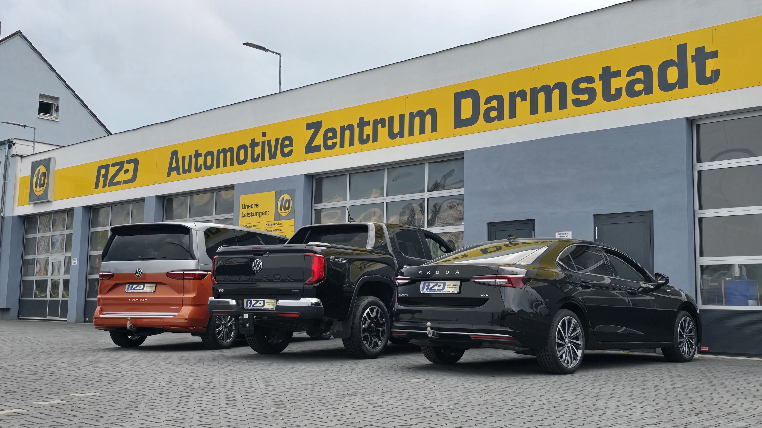 3 geparkte Fahrzeuge (VW T7, VW Amarok, Skoda Superb Limo) mit einer Anhängerkupplung ausgestattet stehen vor der Halle ausge